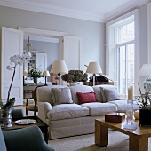 A coffee table and a light upholstered sofa in a living room with a view through open swing doors