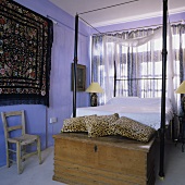 A Mediterranean bedroom - a wooden chest with leopard-print cushions in front of a metal four-poster bed