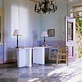 Table lamps with white shades on a desk with angled legs in a Mediterranean-style blue-coloured living room with a chess-board floor