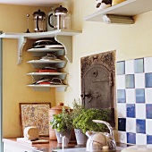 A corner of a kitchen with a light grey shelf and pots of herbs on the work surface