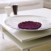Violet beads in a shiny dish on a white coffee table