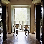 An antique wooden bench in front of open window shutters in the hallway of an old Spanish country house