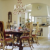 Gedeckter Tisch mit gepolsterten Landhausstühlen und Kerzenleuchter vor offener Küche im Mediterraner Stil