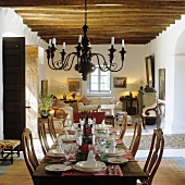 A chandelier hanging from a wooden beamed ceiling above a festively laid dining table in an open plan living-room-cum-dining-room