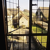 A view through a window onto a courtyard with flagstones and a lawn in front of an English country house