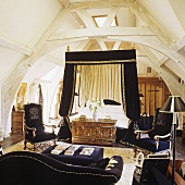 A four poster bed with a black canopy and a black sofa in a converted attic bedroom with trusses