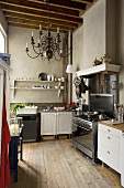 An old kitchen featuring a mixture of styles with grey walls and a chandelier hanging from the rustic wood beam ceiling