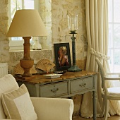 A rustic table lamp with a white shade in a country house-style wall table in front of a plastered natural stone wall