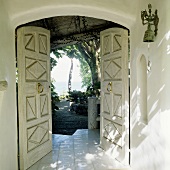 An open front door of a tropical villa with a view of a garden and the sea