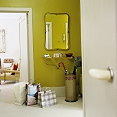 Shopping bags in front of an open door and a hall mirror with a brass shelf below it on a green-painted wall