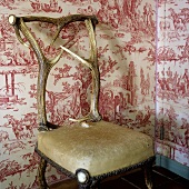 Upholstered chair made of antlers in front of patterned wallpaper on a wall