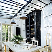 Essplatz und schwarzer hoher Geschirrschrank im Vintagelook im Glasanbau mit offener Gartentür
