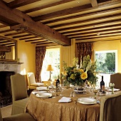 A table laid in a room with a wood beam ceiling in a yellow-painted living room in a country house