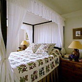 A four poster bed with a white canopy, a floral throw and matching cushions