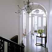 Medusa chandelier in an elegant stairwell with rounded arches and a view of a antique side table in an entrance to a home