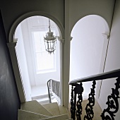 A steep flight of stairs with archways at the bottom with a view of a ceiling lantern