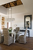 Wicker chairs around a laid table with a crystal chandelier hanging above it