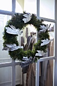 Silver angels on a Christmas wreath hanging on a glazed door to a cloakroom