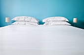 A bed with white bedclothes and pillows against a blue wall