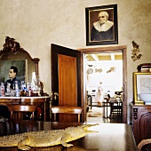 Wohnraum im südafrikanischen Landhaus - ausgestopftes Krokodil auf Tisch und Familienportraits an Wand und offener Küchentür