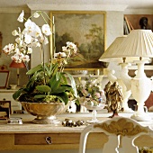 White orchids in a silver bowl and white table lamps on a wooden table