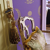 Silk pillows on a vintage wooden chair in front of purple wallpaper with gold colored Oriental pattern