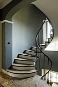 A stairway with a curved hand rail and a dark grey wall in a country house