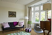 A black leather sofa, a white floor lamp and a curved window bank with a view