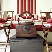 A stack of antique wooden trunks at the end of a bed with red and white striped cover