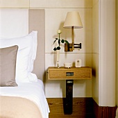 A bedside table with a drawer and a dark wooden foot in front of a white wood panelled wall