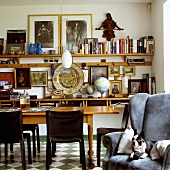 A dog lying in an armchair and a dining table in a living room in front of a wall shelf