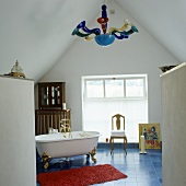 Free standing antique bathtub on blue tile floor in front of a gable wall with a window