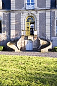 A view across a lawn of a country house with a curved stairway to the front door