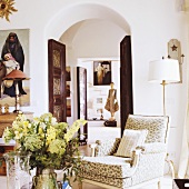 A view through a rounded archway in a Mediterranean house with an upholstered armchair in the anteroom