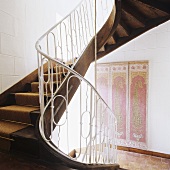 A curved wooden stairway with a white metal banister