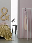 A lamp on a bedside table between a bed and a room divider with a clothes rack