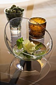 Stillleben - Glasschale mit weisser Rosenblüte und Windlicht neben Oliven im Glas
