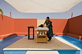 Massage unter Mediterraner Himmel - Frau in Behandlung unter Sonnensegel und Abschirmung mit roter Wand