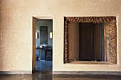 A narrow doorway with a view into a bathroom and an unglazed window with a rustic, natural stone frame