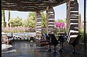 Mediterraner Garten - überdachte Terrasse mit schwarzen Kunststoffstühlen auf poliertem Betonboden