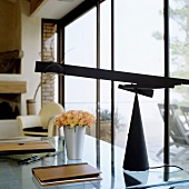 A desk with a glass surface and a black desk lamp in front of a window