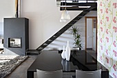 Offener Wohn- und Essraum mit schwarz glänzendem Tisch vor Treppe und Kaminofen