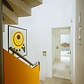 A stairway with a banister rail mounted on an orange panel and a view through an open door into the hallway