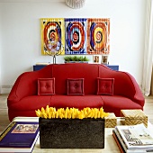 Yellow tulips in a black vase in front of a curved red sofa with a picture hanging on the wall behind it