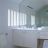 A white bathroom in an attic - a wash basin with a built-in cupboard and a full-wall mirror