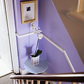 Blick auf Treppenpodest mit Tisch und Orchidee vor fliederfarbener Wand
