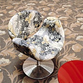 A floral pattern on an upholstered designer chair with a metal foots and a floral carpet