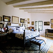 A bed with a blue and white quilt and an upholstered bench in a bedroom in Mediterranean country house with a wood beam ceiling