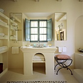 A Mediterranean bathroom - a stone washstand with an arched base and a window with blue shutters on the inside