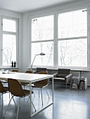 Tisch mit braunen Stühlen und Sesseln vor Fensterfront